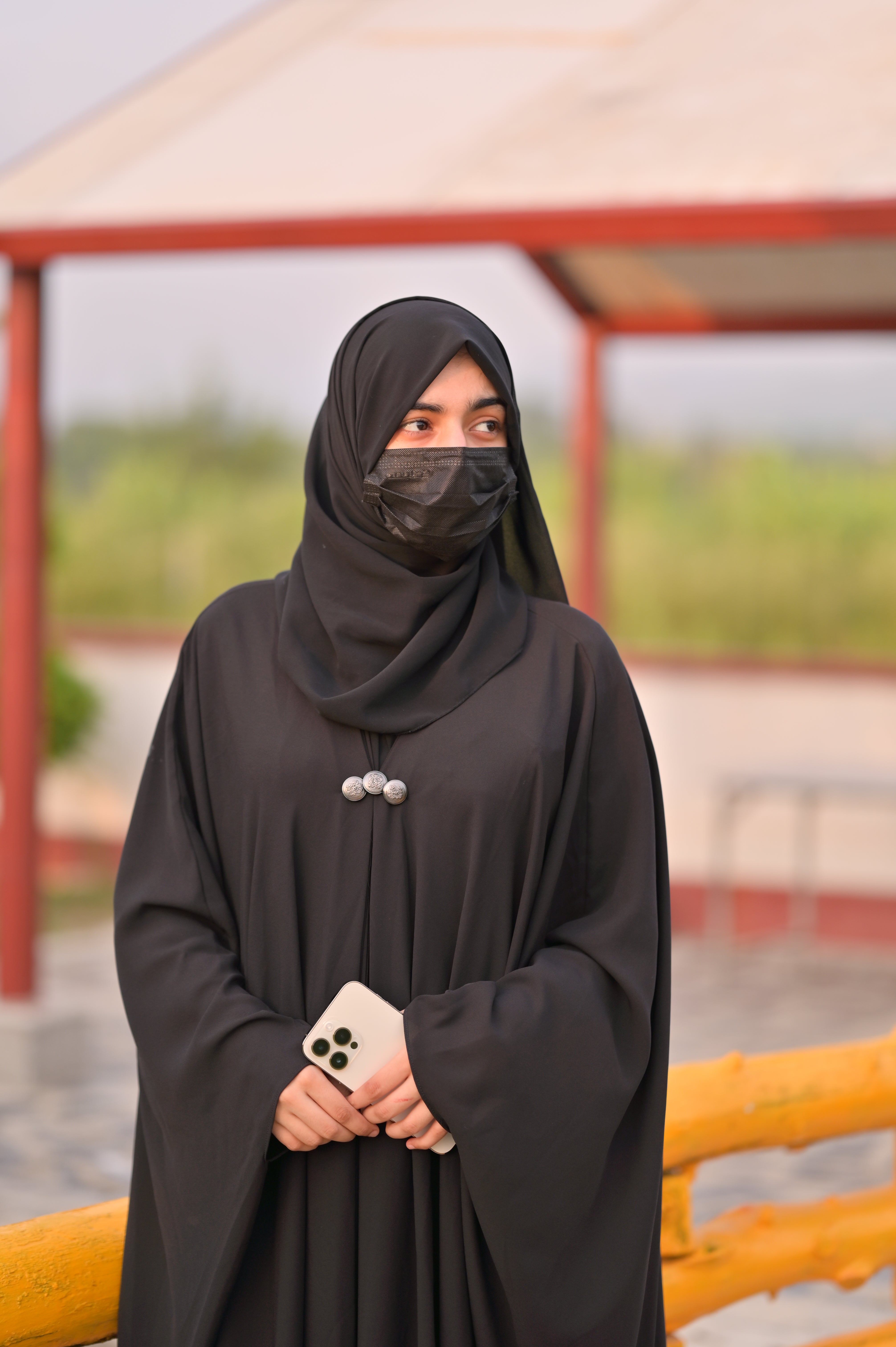 Woman wearing black abaya with matching scarf and holding a smartphone outdoors