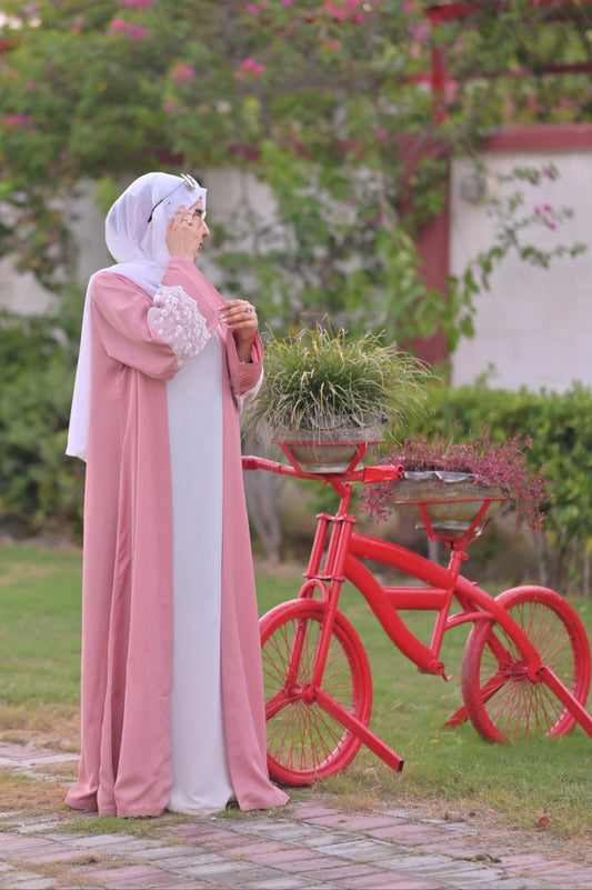 Clarity Glam luxury abaya with scarf in pink and white party wear standing next to decorative red bicycle planter