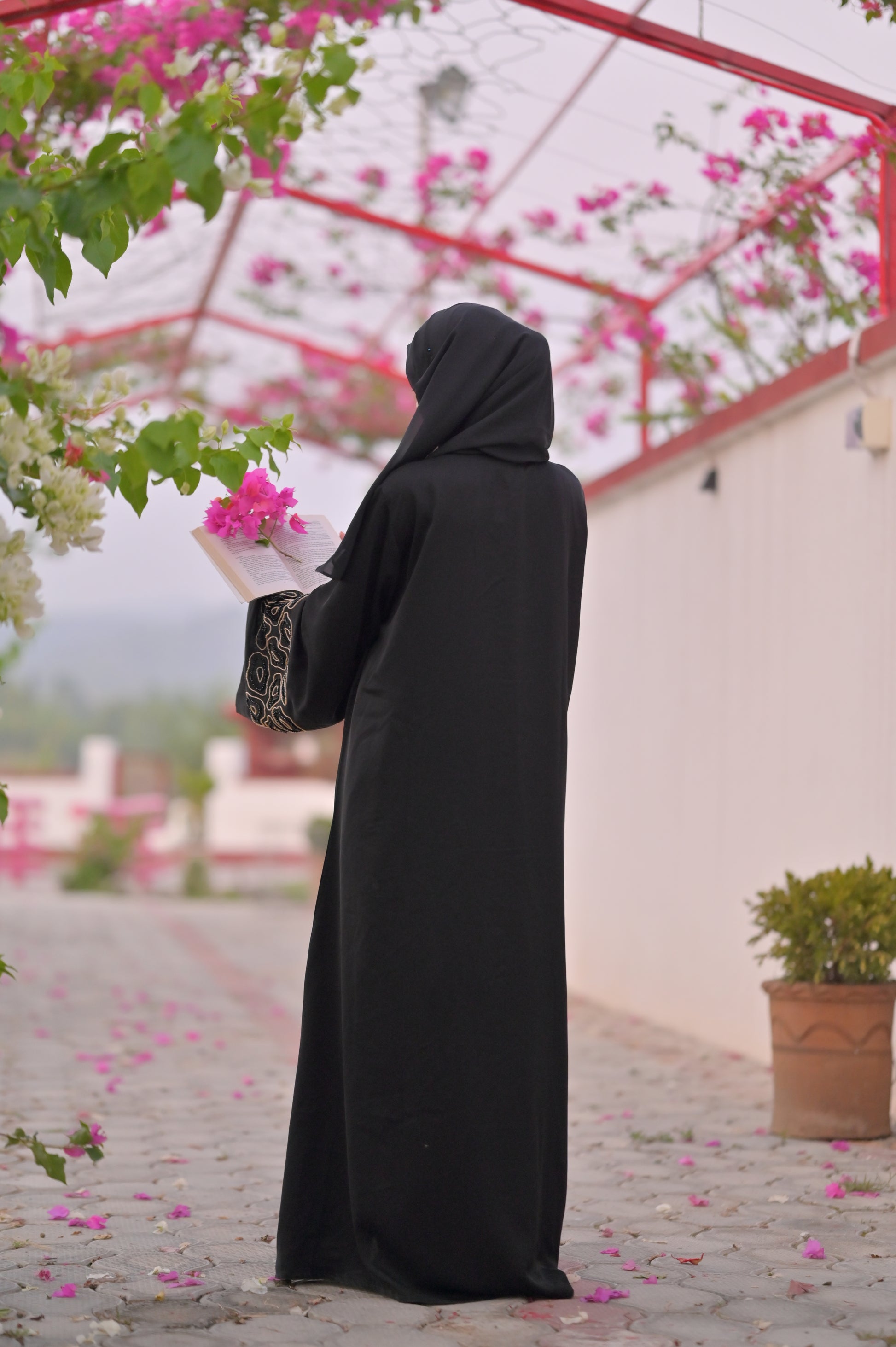 Woman wearing luxury black abaya with intricate sleeve details standing outdoors under flowering trellis