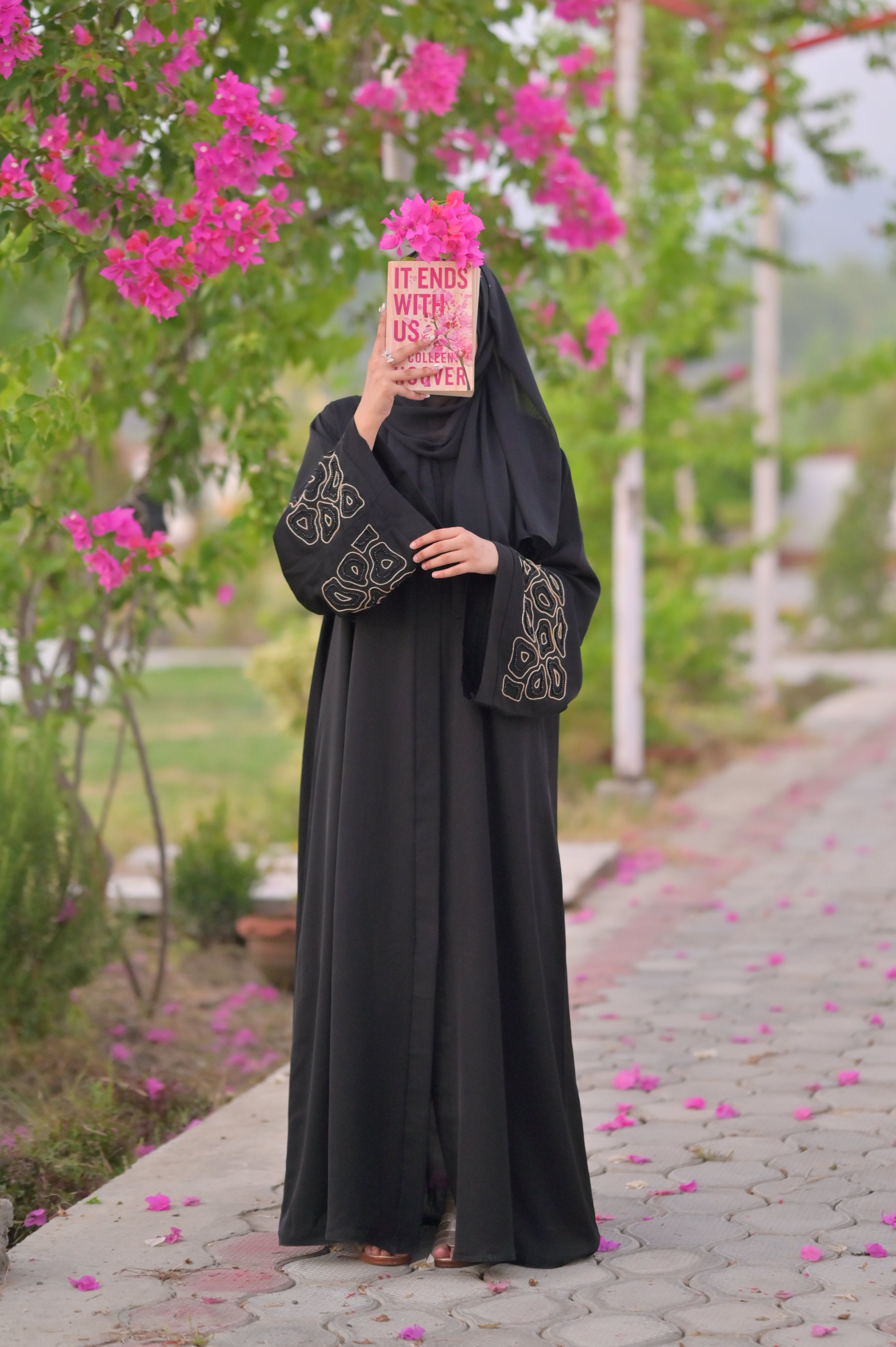 Woman wearing luxury black abaya with intricate sleeve embroidery standing outdoors holding a book
